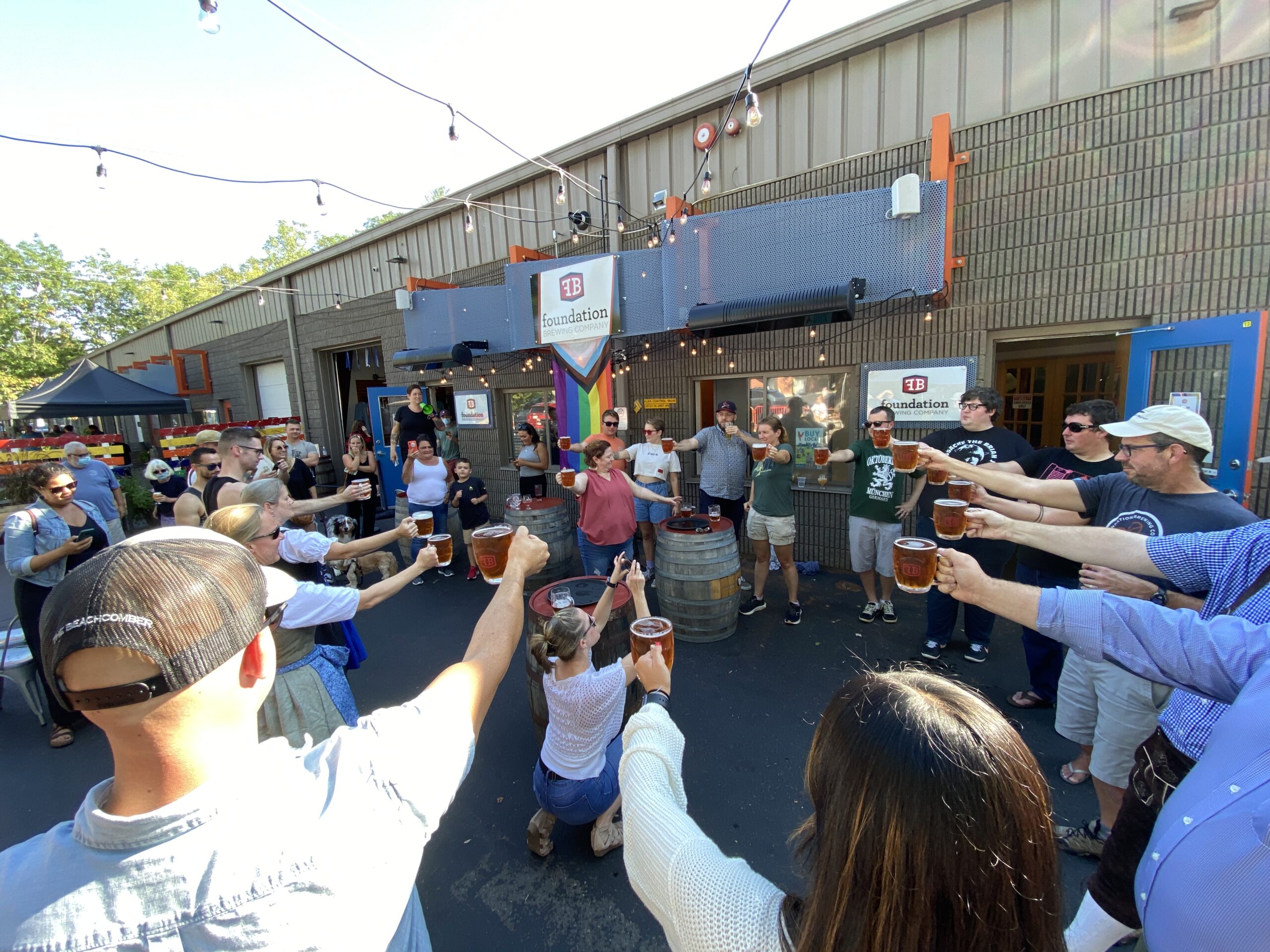 Group of people holding beer steins in front of brewery.